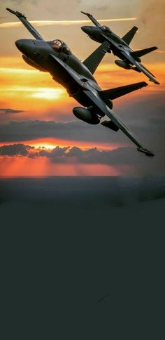 two fighter jets flying in the sky at sunset