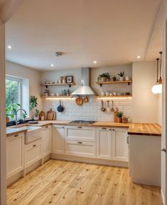 a kitchen with wooden floors and white cabinets, potted plants on the shelf above the stove