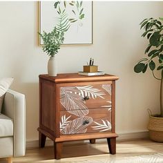 a small wooden cabinet with leaves painted on the front and sides, next to a white couch