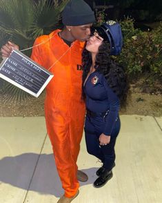 a man in an orange jumpsuit kissing a woman with a chalkboard attached to her chest