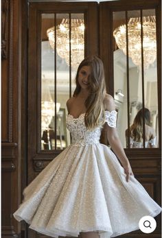 a woman standing in front of a wooden door wearing a short white dress with sequins on it