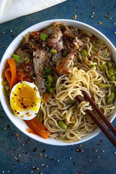 a bowl filled with noodles, meat and veggies next to chopsticks