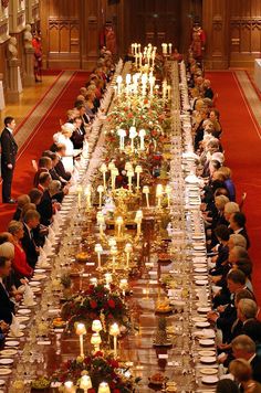 a long table with many people sitting at it and candles on the tables in front of them