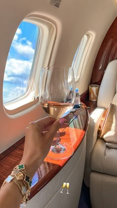 a person holding a glass of wine in front of an airplane window with the seat down