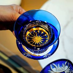 a hand is holding a blue glass with gold decorations on it and the bottom part of the glass has a ring in it