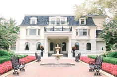 a large white house with a fountain in front of it and lots of pink flowers