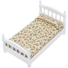 a white doll bed with floral sheets and pillowcases on it's sides