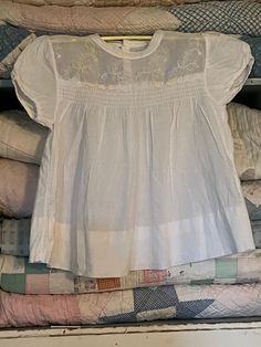 "This adorable vintage baby dress is white cotton with sweet yellow embroidered flowers. There's smocking on the front and measures approximately 12\" from the shoulders to the hem. There's no tag but I would say it would fit 12 months? It has been washed and ironed and has a button closure on the back with no stains or tears." White Cotton Blouse With Smocked Bodice, Vintage Smocked Bodice Top For Summer, Vintage Summer Tops With Smocked Bodice, Cotton Tops For Baptism In Spring, White Smocked Short Sleeve Blouse, Fitted Top For Baptism In Spring, Fitted Tops For Baptism In Spring, Cotton Baby Dress, Vintage Baby Dress