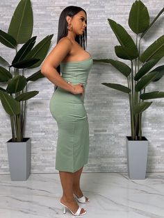 a woman standing in front of two potted plants wearing a strapless green dress