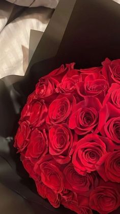 a large bouquet of red roses in a black paper wrapper on a white sheet