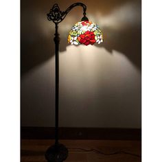 a lamp that is on top of a wooden floor next to a wall with a flowered glass shade