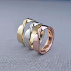 three different colored gold and silver rings on a gray surface with one ring in the middle