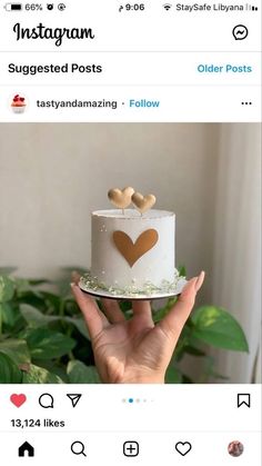 someone is holding up a white cake with hearts on the top and two gold hearts on the bottom