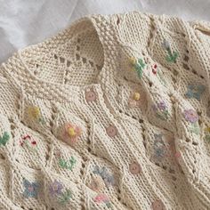 a crocheted sweater with flowers and leaves on the front is laying on a white sheet