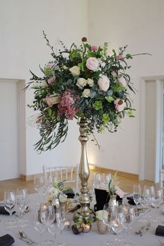 a tall silver vase filled with flowers on top of a table covered in wine glasses