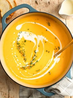 a blue pot filled with soup on top of a wooden table next to slices of bread