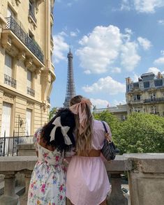 two women standing next to each other in front of the eiffel tower