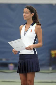 a female tennis player in a white shirt and blue skirt holding a piece of paper