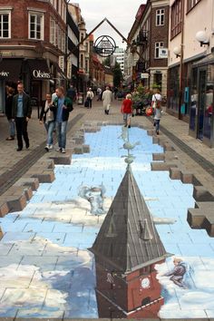 people are walking down the street with an artistic painting on it's sidewalk in front of buildings