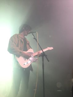 a man standing in front of a microphone while holding a guitar