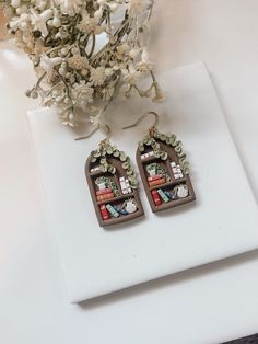 a pair of earrings sitting on top of a white table next to a vase with flowers