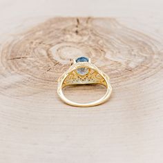 a gold ring with a blue stone in the center on top of a piece of wood