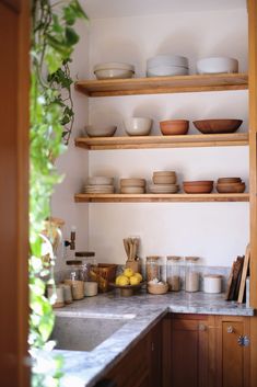 a kitchen with wooden shelves filled with dishes and bowls on top of each shelf next to a sink