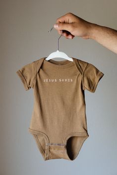 someone is holding up a baby's bodysuit with the word jesus saves on it