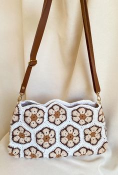 a crocheted purse sitting on top of a white cloth covered tablecloth with a brown leather strap