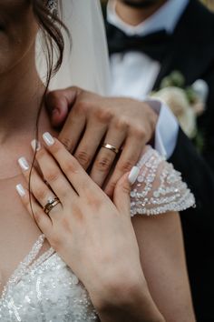 the bride and groom are holding each other's wedding rings while they stand close together