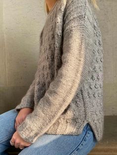 a woman sitting on the floor wearing jeans and a sweater