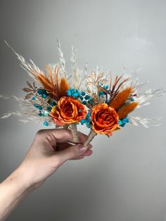 a hand holding two flowers with feathers on it's stems and one flower is orange