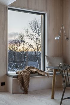 a window seat with a blanket on it next to a table and chair in front of the window