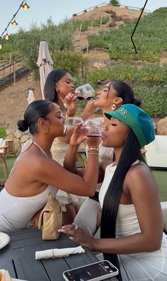 three women sitting at a table drinking from wine glasses and looking up into the sky