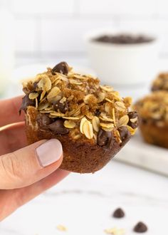 a person holding up a muffin with chocolate chips and oats on the top