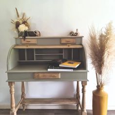 an old desk with some books on it and a vase full of flowers next to it