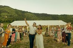 a group of people standing around each other in front of a tent with string lights