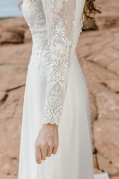 a woman in a white wedding dress holding her hand out to the side while standing on rocks