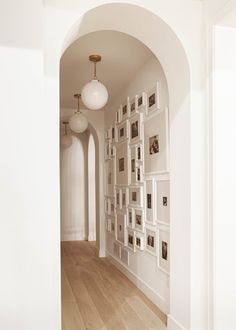 an archway leading into a white room with pictures on the wall and wooden flooring