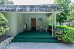 two lawn chairs sitting in front of a small shed with green grass and bushes around it