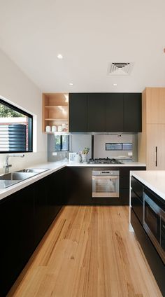 a modern kitchen with black cabinets and white counter tops, wood flooring and stainless steel appliances