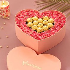 a heart shaped box filled with chocolates next to a candle and some flowers on a table