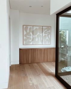 an empty room with wooden floors and artwork on the wall above it, in front of a sliding glass door