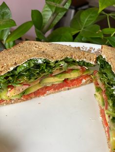 a sandwich cut in half sitting on top of a white plate next to a potted plant