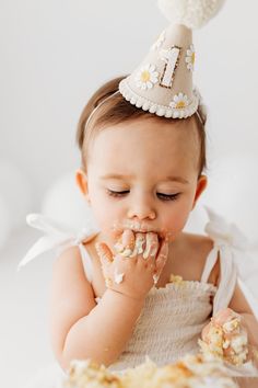 a baby girl wearing a party hat eating cake with her hands and face covered in frosting