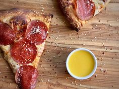 two slices of pepperoni pizza next to a small bowl of mustard