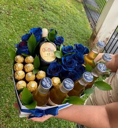 a person holding a box filled with blue roses and bottles of beer next to some chocolates