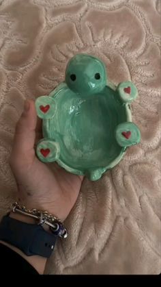 a hand holding a green turtle shaped bowl with hearts on it's sides and the lid