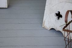 the corner of a porch with a clock on it's side and an iron planter next to it