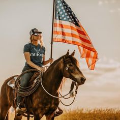 a woman riding on the back of a brown horse holding an american flag